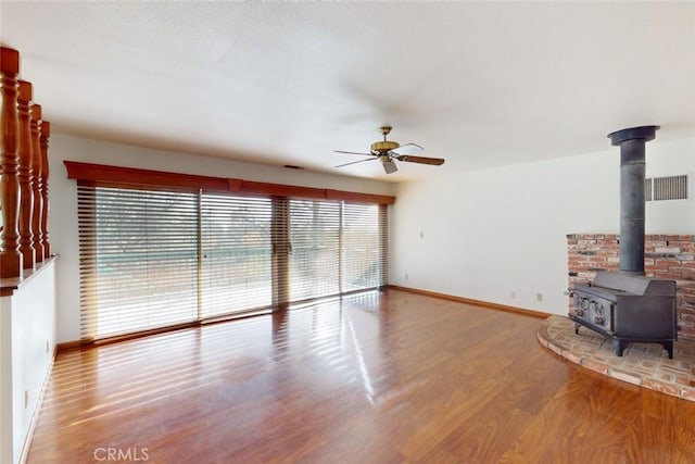 unfurnished living room featuring wood-type flooring, a wood stove, and ceiling fan