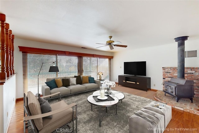 living room with a wood stove, ceiling fan, and hardwood / wood-style flooring