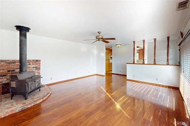 unfurnished living room featuring a wood stove, ceiling fan, and hardwood / wood-style flooring