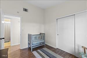 bedroom with dark hardwood / wood-style flooring, a closet, and a crib