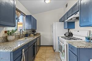 kitchen featuring appliances with stainless steel finishes, vaulted ceiling, blue cabinets, sink, and light tile patterned floors