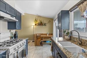 kitchen with sink, light stone counters, stainless steel range oven, vaulted ceiling, and light tile patterned flooring