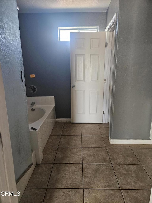 bathroom with tile patterned flooring, a relaxing tiled tub, and a textured ceiling