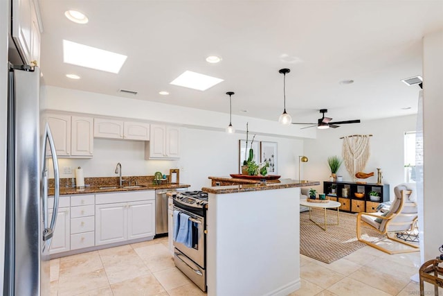 kitchen featuring appliances with stainless steel finishes, sink, white cabinets, dark stone counters, and hanging light fixtures