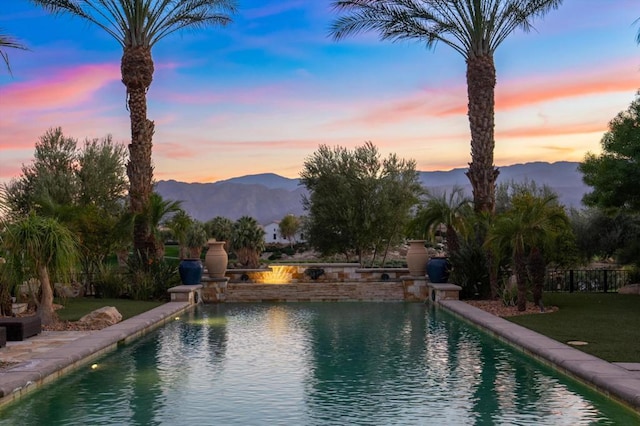 pool at dusk with a mountain view and a yard