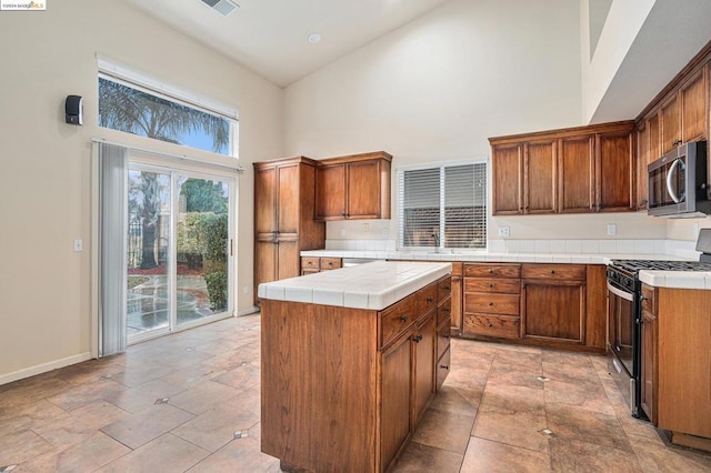 kitchen featuring a high ceiling, range with gas stovetop, a kitchen island, sink, and tile countertops