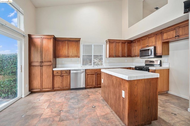 kitchen featuring a towering ceiling, appliances with stainless steel finishes, tile countertops, and a kitchen island