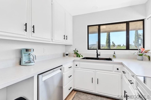 kitchen featuring stainless steel dishwasher, white cabinetry, sink, and hardwood / wood-style flooring