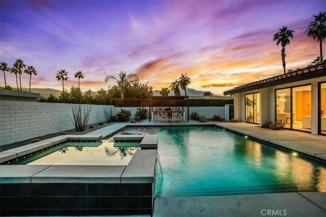 pool at dusk featuring an in ground hot tub and a patio area