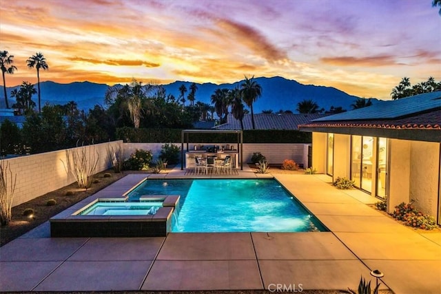 pool at dusk featuring an in ground hot tub, a mountain view, and a patio area