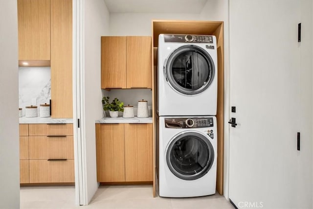 laundry area featuring cabinets, stacked washing maching and dryer, and light tile patterned floors