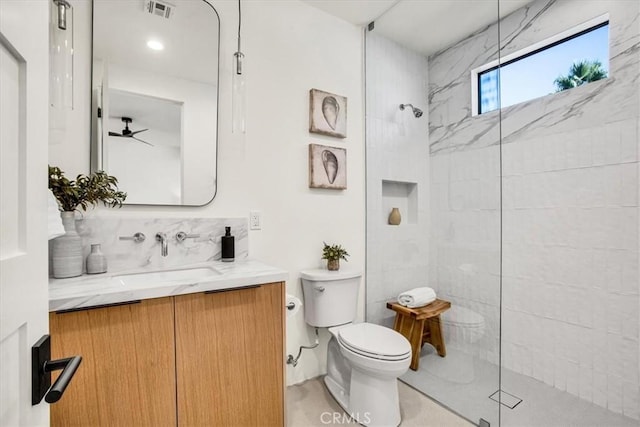 bathroom with ceiling fan, vanity, toilet, and a tile shower