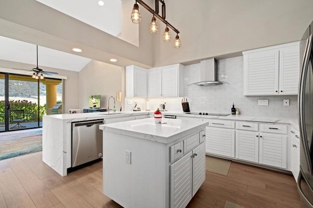 kitchen featuring wall chimney exhaust hood, stainless steel dishwasher, kitchen peninsula, decorative light fixtures, and a kitchen island