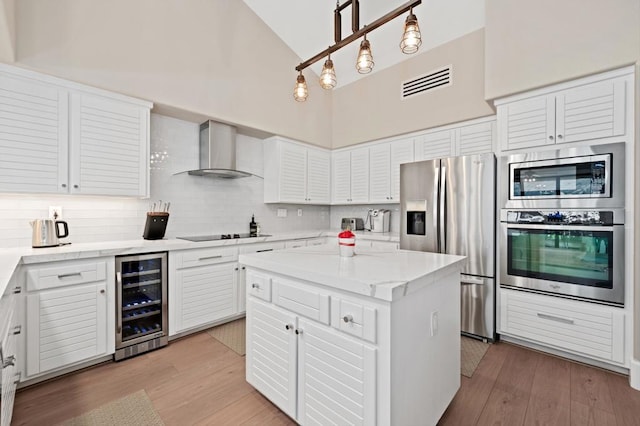 kitchen with white cabinetry, stainless steel appliances, wall chimney range hood, wine cooler, and a kitchen island