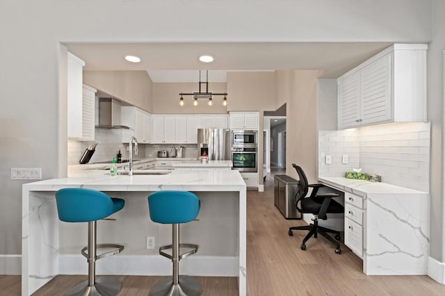 kitchen with white cabinets, wall chimney exhaust hood, kitchen peninsula, and appliances with stainless steel finishes