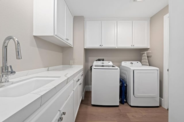 laundry room with cabinets, light wood-type flooring, washing machine and clothes dryer, and sink