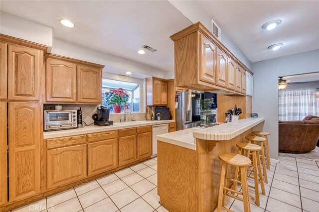 kitchen featuring decorative backsplash, stainless steel refrigerator with ice dispenser, sink, dishwasher, and tile counters