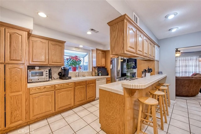 kitchen with tile countertops, stainless steel refrigerator with ice dispenser, tasteful backsplash, white dishwasher, and sink