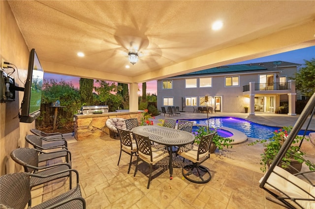 patio terrace at dusk featuring a balcony and exterior kitchen