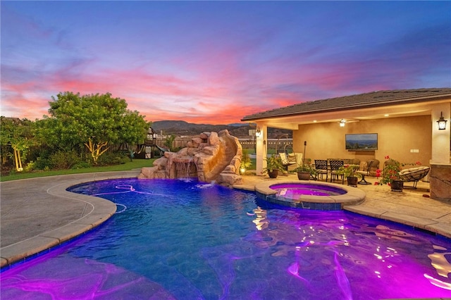 pool at dusk featuring an in ground hot tub, pool water feature, and a patio