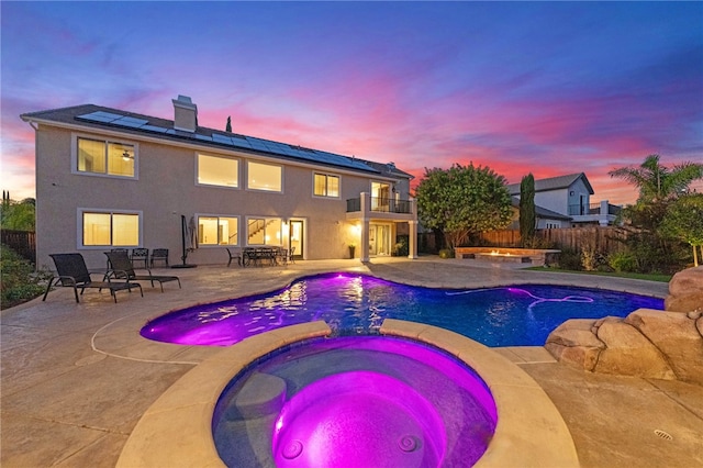 pool at dusk with a patio area and an in ground hot tub