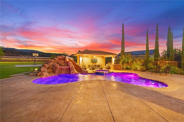 pool at dusk with an in ground hot tub and a patio