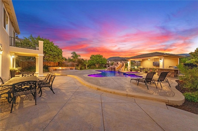 pool at dusk featuring a patio and an outdoor kitchen