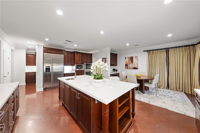 kitchen with dark wood-type flooring, a kitchen island with sink, crown molding, sink, and stainless steel appliances