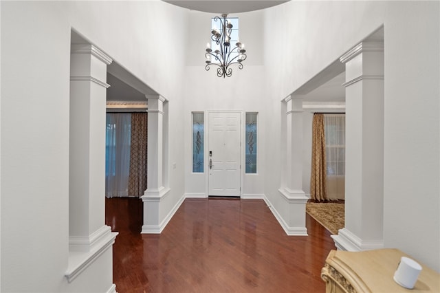 entryway with ornate columns, a towering ceiling, dark hardwood / wood-style floors, and a notable chandelier