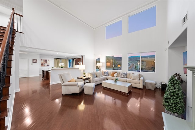 living room with a towering ceiling, dark hardwood / wood-style floors, and ornamental molding