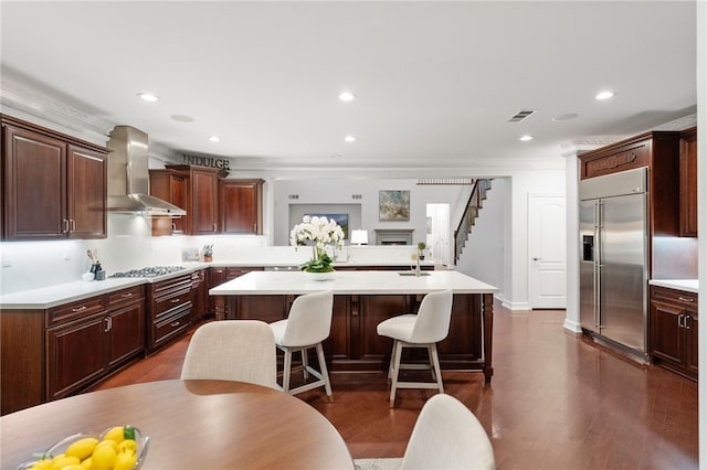 kitchen with a center island, wall chimney exhaust hood, stainless steel appliances, a kitchen breakfast bar, and dark hardwood / wood-style flooring