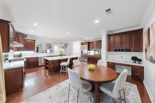 dining area with sink, wood-type flooring, ornamental molding, and decorative columns