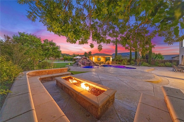 pool at dusk with an outdoor fire pit and a patio area