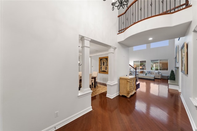 hallway with hardwood / wood-style flooring, a chandelier, a high ceiling, and decorative columns