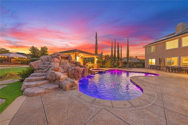 pool at dusk featuring pool water feature and a patio