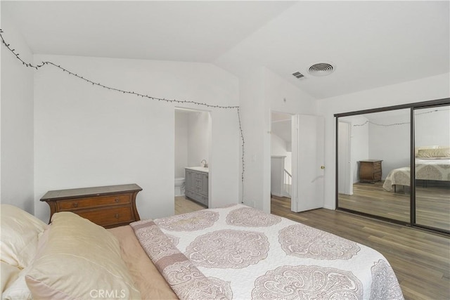 bedroom featuring wood-type flooring, ensuite bathroom, a closet, and lofted ceiling