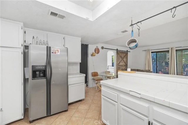 kitchen featuring tile countertops, white cabinets, a barn door, light tile patterned floors, and stainless steel fridge with ice dispenser