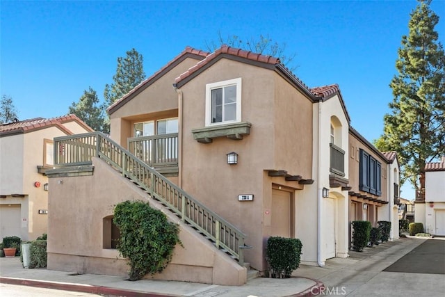 view of side of home featuring a tiled roof, stairway, and stucco siding