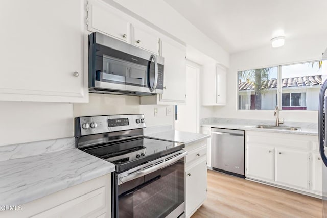 kitchen with appliances with stainless steel finishes, light hardwood / wood-style floors, white cabinetry, and sink