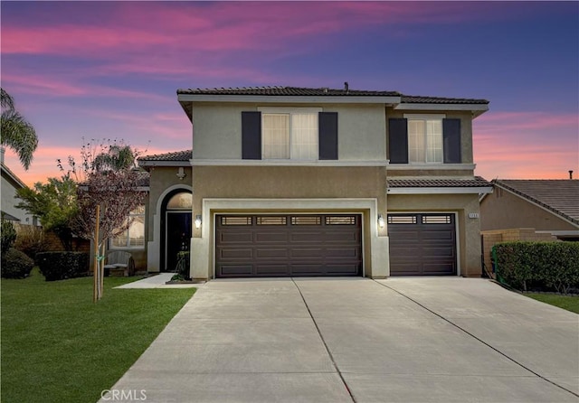 traditional-style house featuring driveway, stucco siding, a garage, a tiled roof, and a lawn