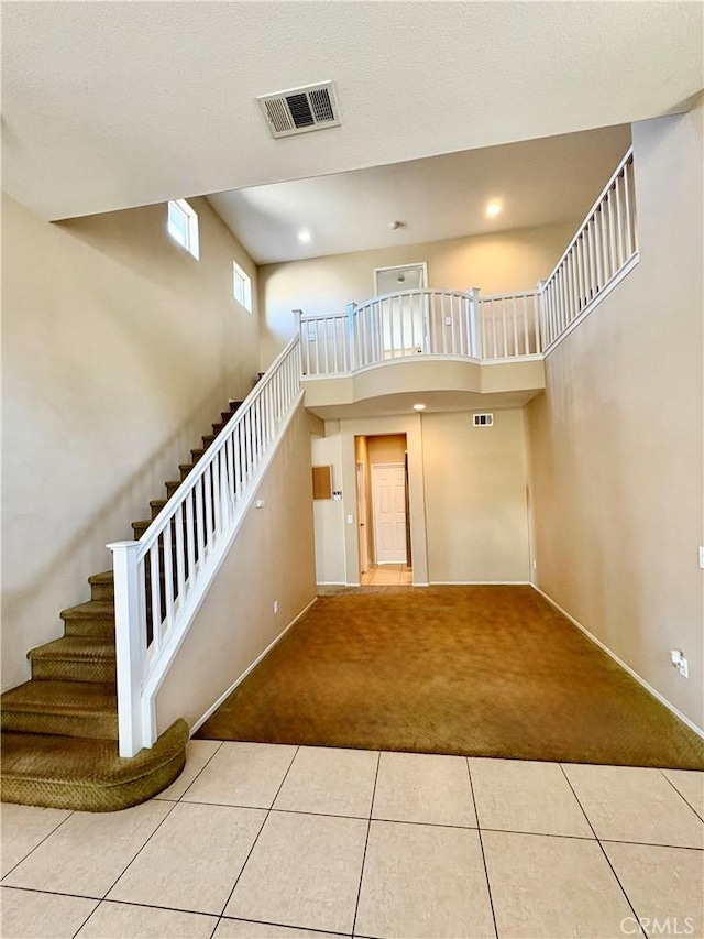 stairway featuring tile patterned floors, visible vents, carpet flooring, baseboards, and a towering ceiling