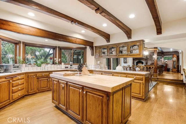 kitchen featuring backsplash, beamed ceiling, a kitchen island, and light hardwood / wood-style floors