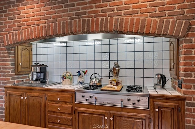 kitchen with tile countertops, stainless steel stovetop, brick wall, and stainless steel gas cooktop