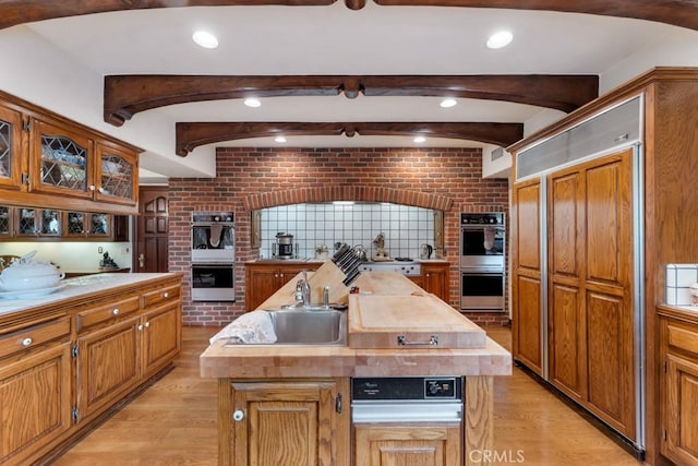 kitchen featuring brick wall, an island with sink, double oven, and light hardwood / wood-style flooring