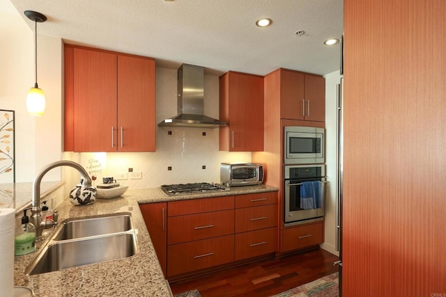 kitchen with pendant lighting, appliances with stainless steel finishes, wall chimney range hood, sink, and dark hardwood / wood-style floors