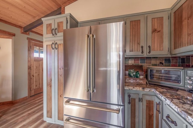 kitchen featuring wooden ceiling, backsplash, high end refrigerator, vaulted ceiling with beams, and light stone countertops