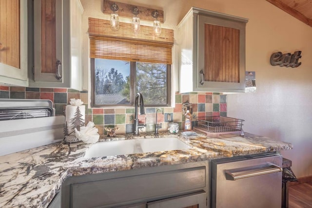 kitchen with decorative backsplash, lofted ceiling, stainless steel dishwasher, light stone counters, and sink