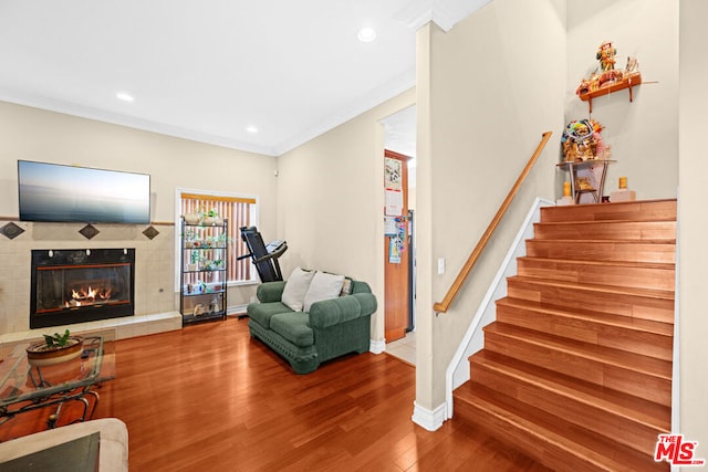 interior space with wood-type flooring, a tile fireplace, and crown molding