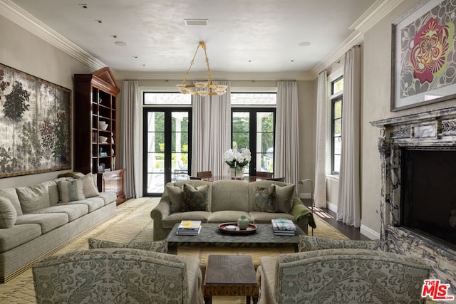 living room with french doors, ornamental molding, a premium fireplace, and an inviting chandelier