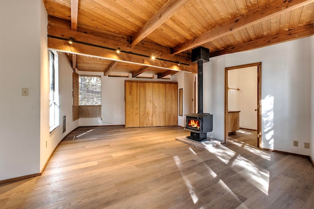 unfurnished living room with beam ceiling, a wood stove, light hardwood / wood-style flooring, and wooden ceiling